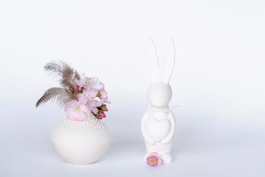 Elegant Easter-themed setup with pink flowers and a white bunny statue on a white background.