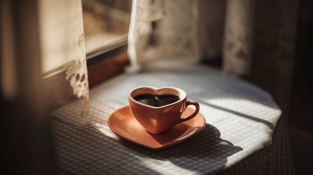 Warm and cozy coffee moment with heart-shaped cup by the window, capturing soft sunlight.