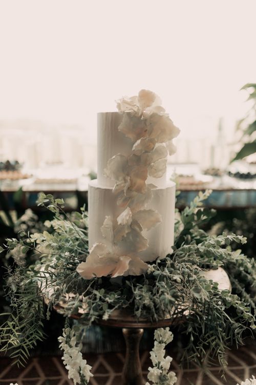 Free A two-tier white wedding cake adorned with delicate flowers and greenery, perfect for elegant celebrations. Stock Photo