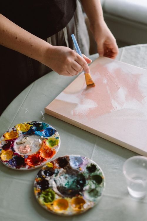 Free A female artist works on an abstract painting with vibrant colors on a sunlit studio table. Stock Photo