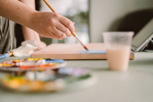Free Artist applying blue paint on canvas in a sunlit home studio. Creative workspace ambiance. Stock Photo