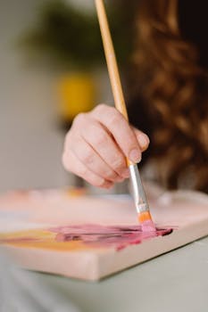 A close-up of a female artist's hand painting on a canvas with natural light.