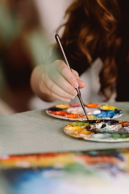 Free Close-up of a female artist painting with vibrant colors in a sunlit home studio. Stock Photo