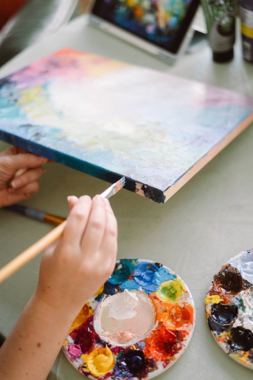 Free An artist paints a vibrant canvas in natural light, surrounded by colorful palettes. Stock Photo