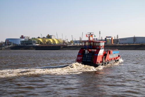 Free A ferry sails on the Elbe River near Hamburg's port, with clear skies and waterfront buildings. Stock Photo