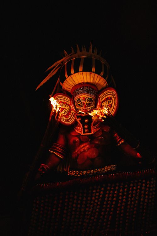 Free A vibrant Theyyam performer with intricate face paint and flames during a ritualistic dance at night. Stock Photo
