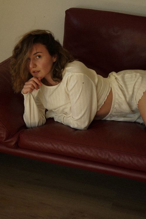 Free A woman in casual attire poses on a red leather couch in an indoor setting, exuding a relaxed and intimate vibe. Stock Photo