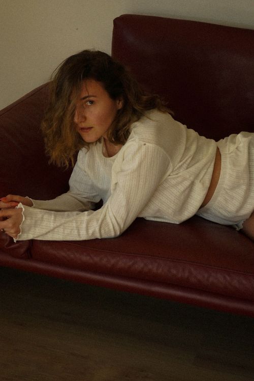 Free Young woman in cozy white outfit lounging on a red leather sofa indoors, exuding calm and relaxation. Stock Photo