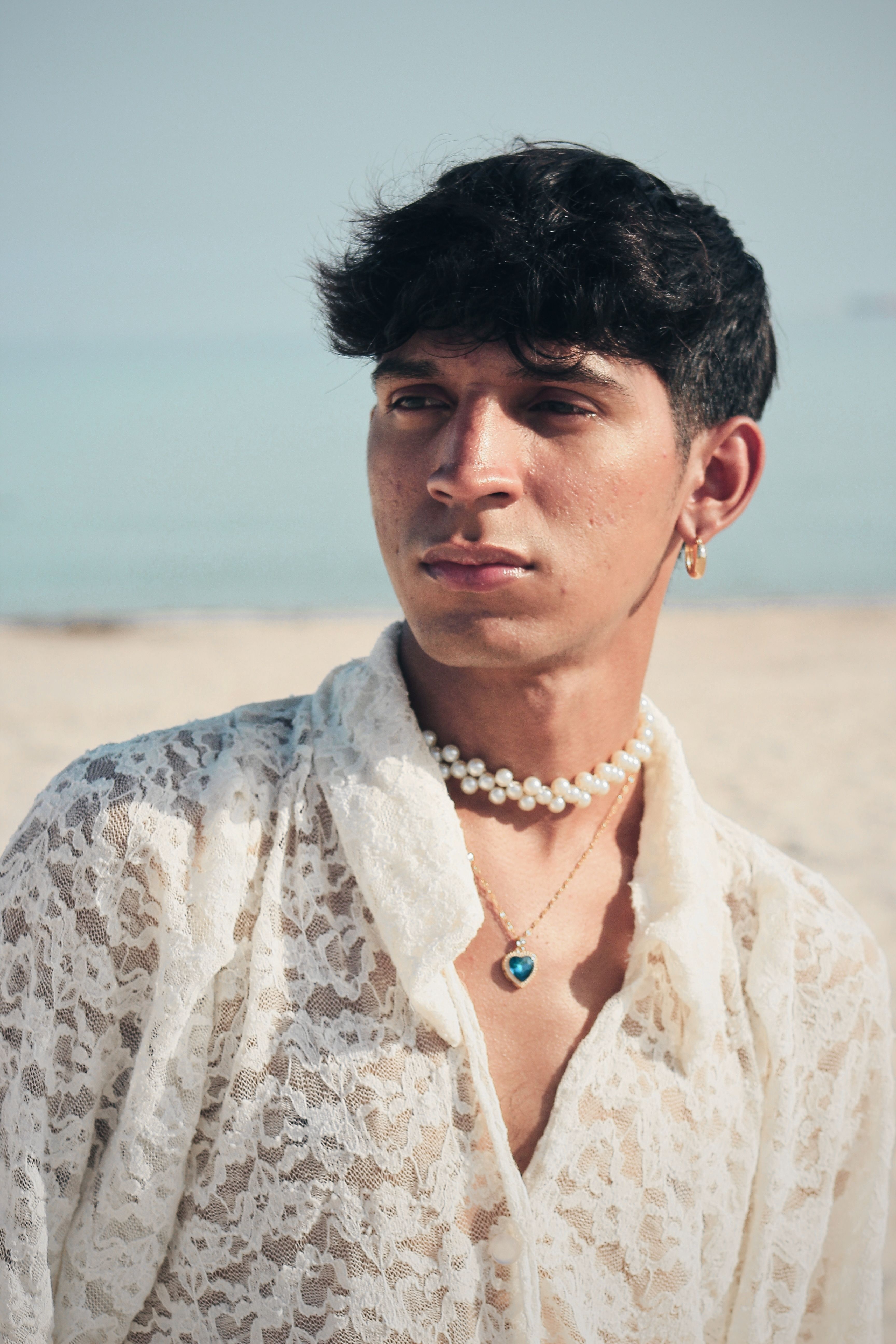 Young adult wearing lace clothing and pearl jewelry on a sunny beach.