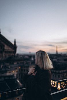 A woman looks over Paris at dusk, with Eiffel Tower in the distance.