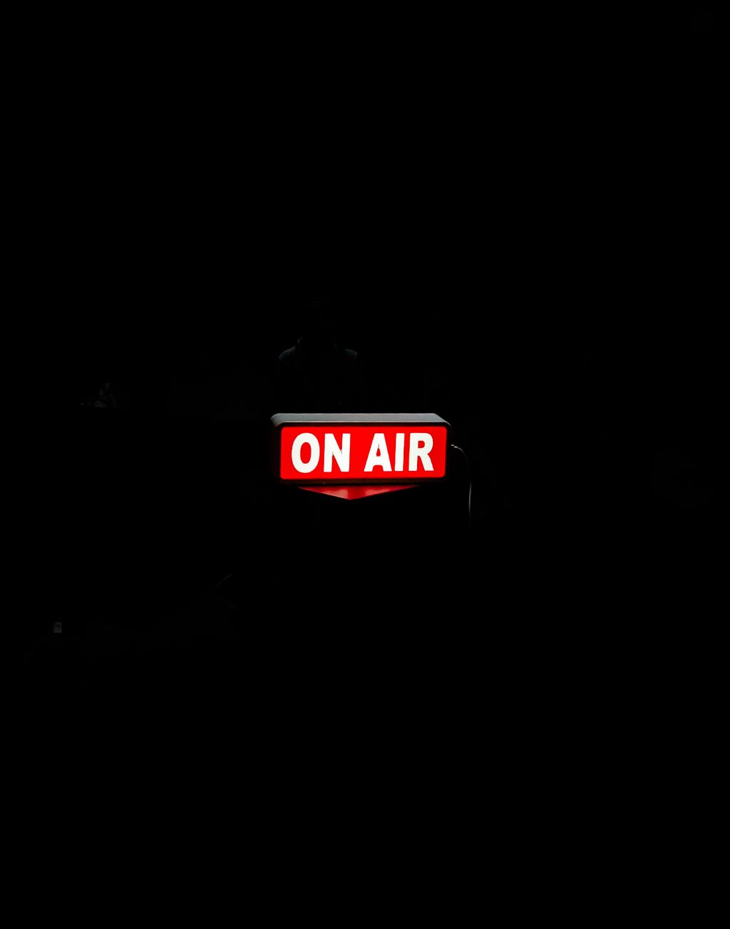Een fel 'On Air'-bord gloeit in de donkere studio en creëert een sfeervolle sfeer.