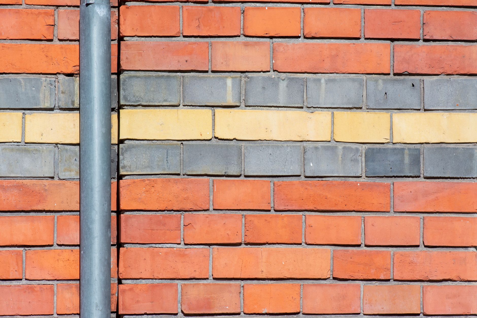 Vibrant brick wall featuring red, yellow, and gray bricks with a metal drainpipe.