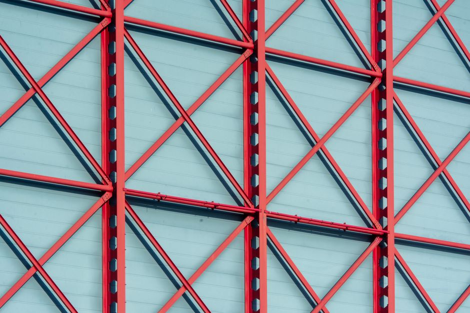 Dynamic red steel beams crisscross against a blue backdrop, creating a geometric pattern.