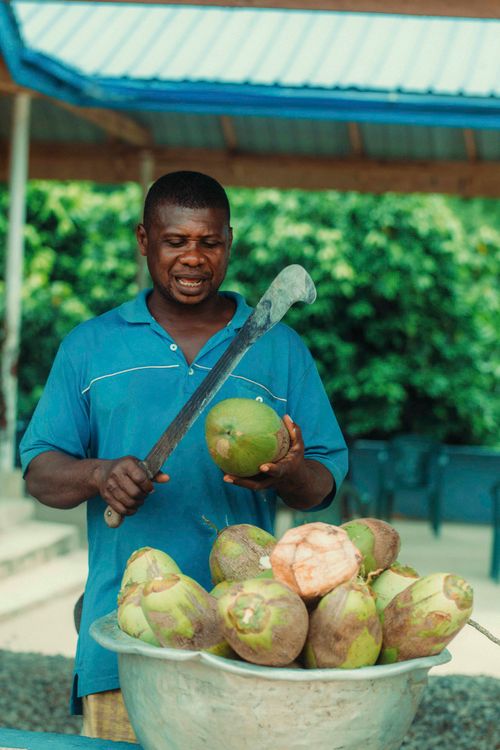 Free Local vendor cutting fresh coconuts in a Ghanaian market, showcasing traditional food preparation. Stock Photo