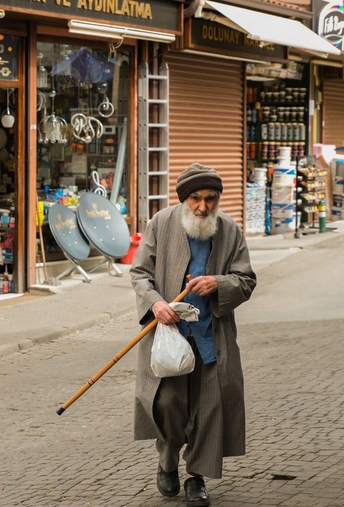 Free Elderly man in traditional attire walks through a bustling market with a cane, showcasing daily life. Stock Photo