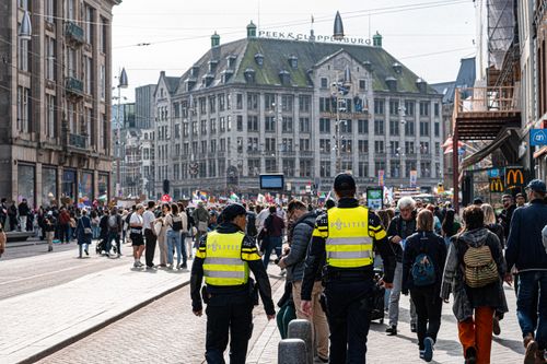Free A bustling European street with police officers and diverse crowd under a sunny sky. Stock Photo