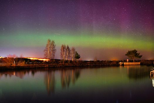 Vibrant aurora borealis illuminates the night sky over a tranquil lakeside scene.