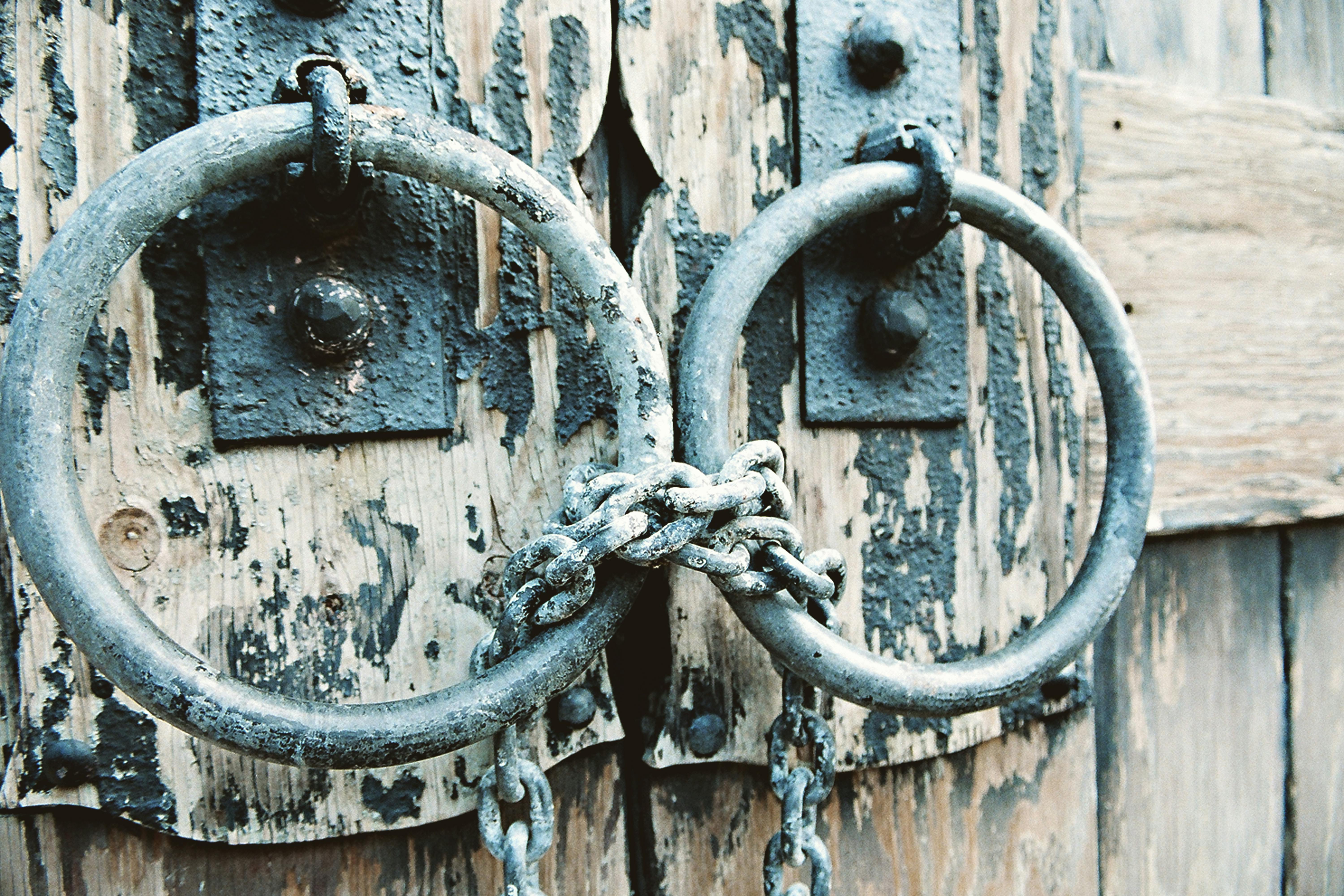 Close-up of a weathered wooden door with metal rings and chains creating a rustic texture.