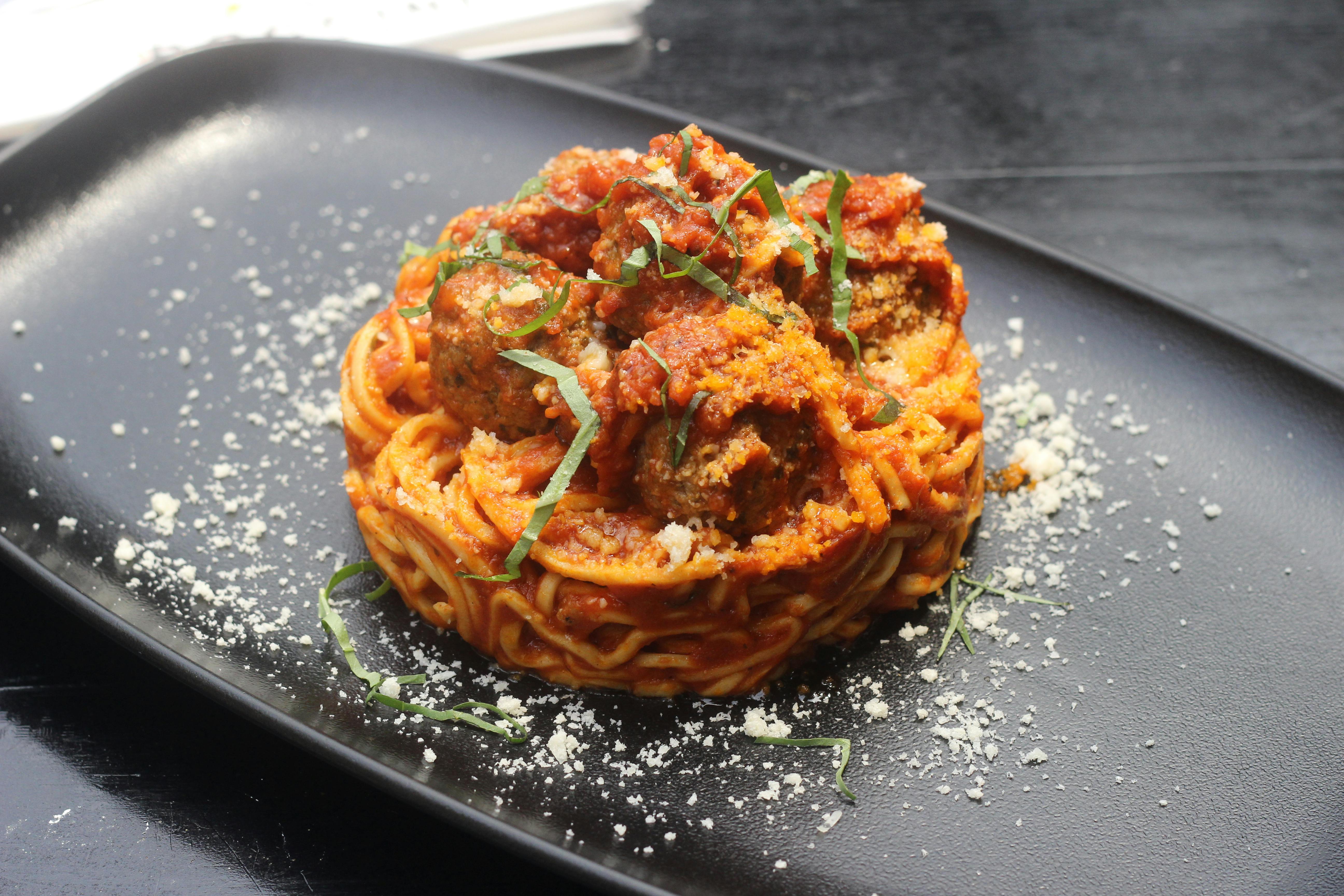 A serving of spaghetti with meatballs topped with basil on a black plate.