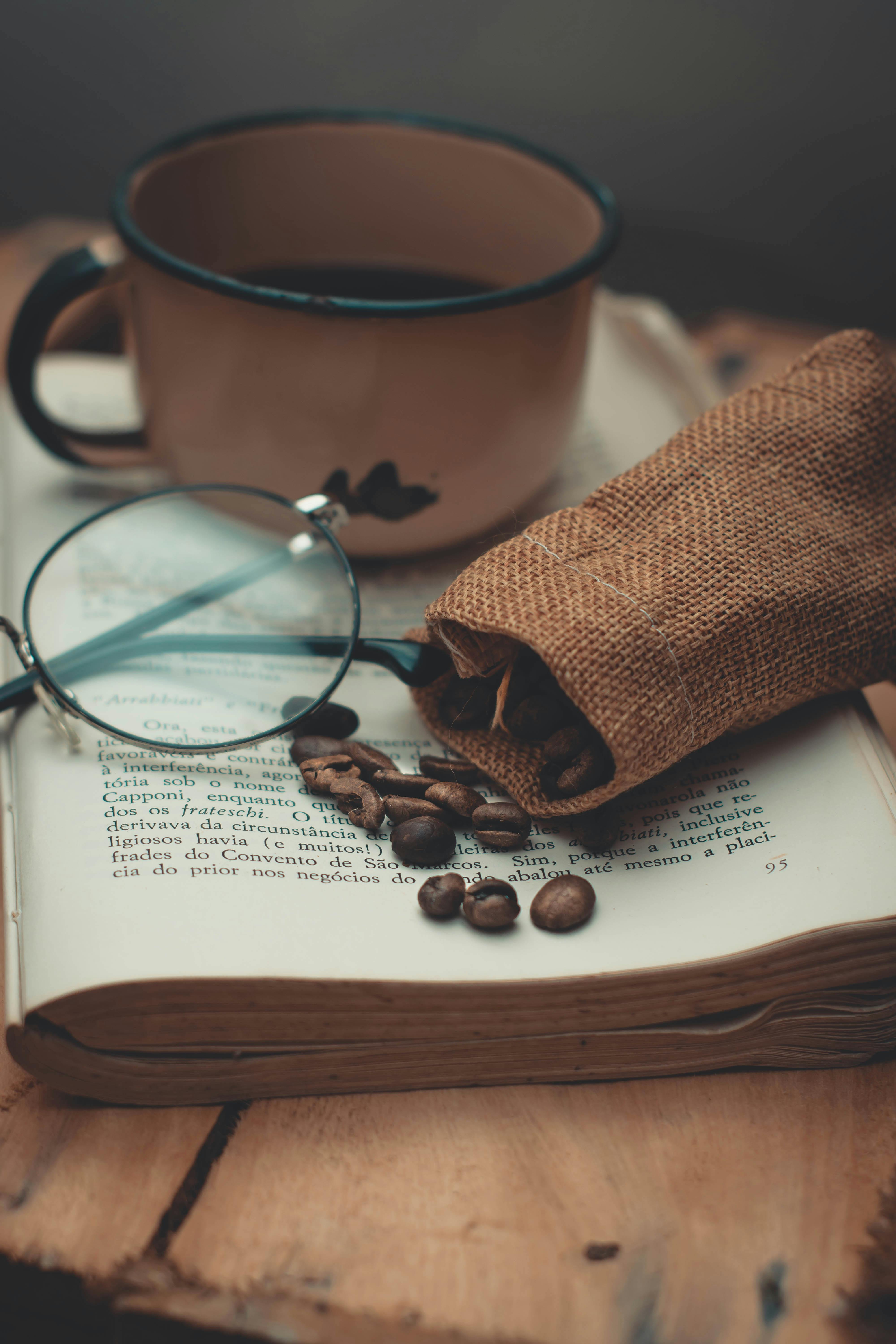 质朴的环境中，木桌上放着一杯热气腾腾的咖啡、一本书和一些散落的咖啡豆
