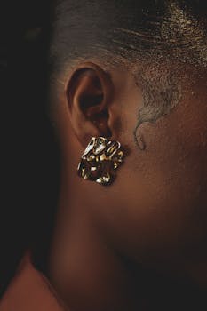 Close-up of a woman wearing a stylish, artistic gold earring against a dark background.