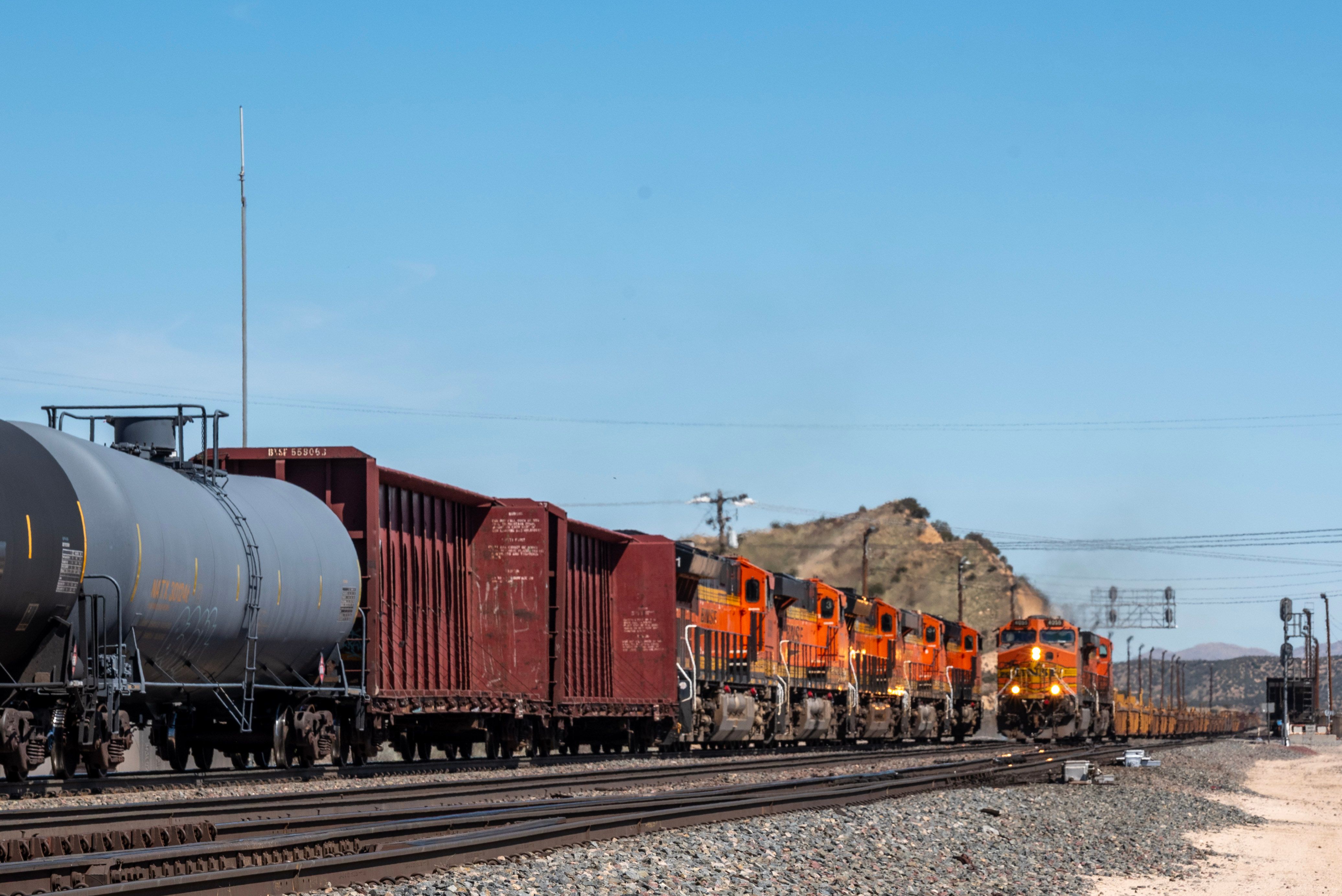 Row of vibrant cargo containers on train tracks under a clear blue sky.