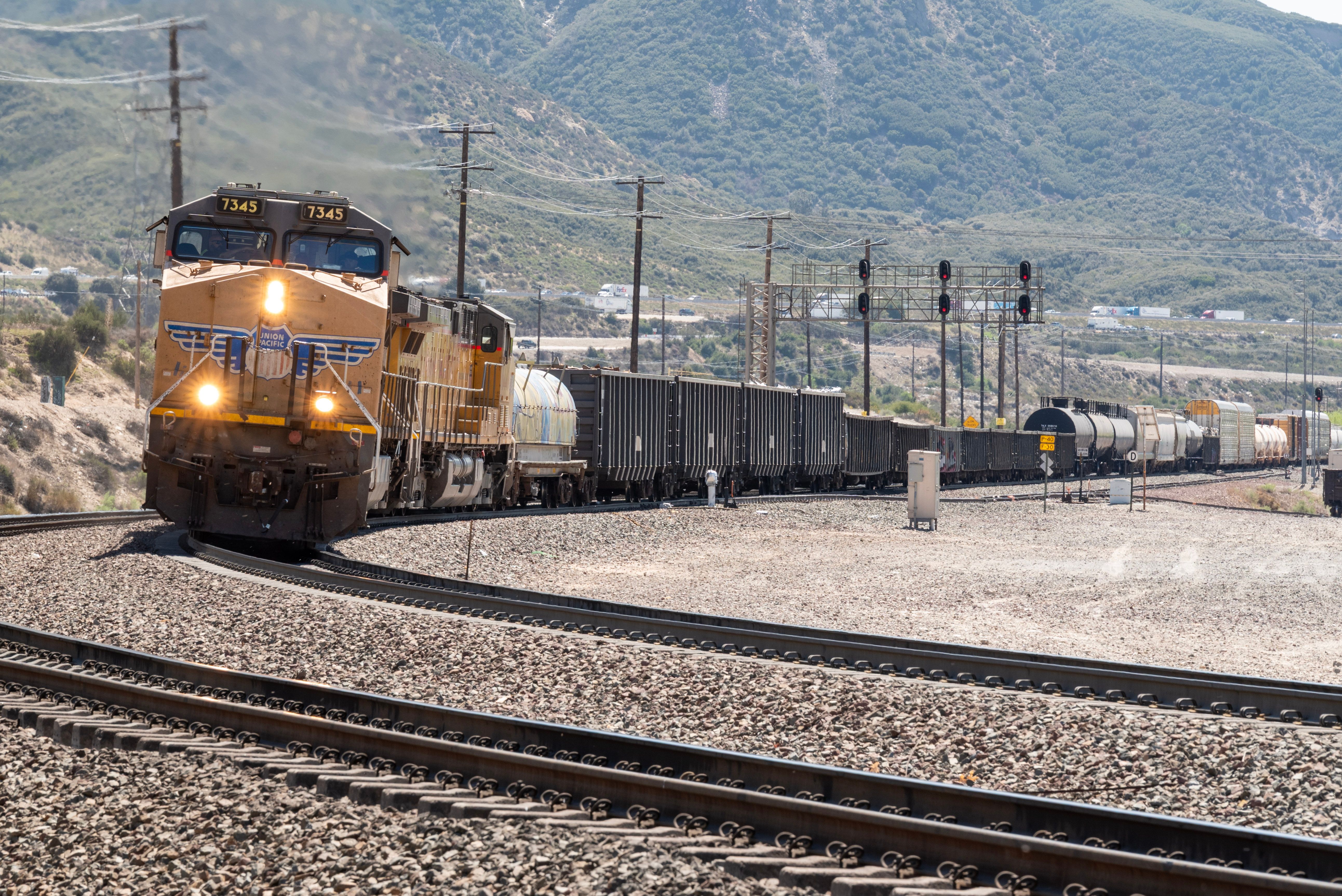 A freight train travels through scenic mountainous terrain on a bright sunny day.