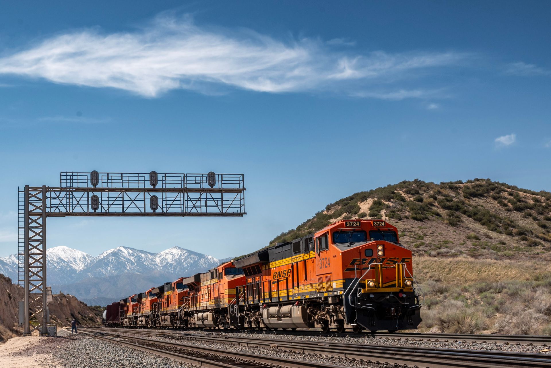 Freight train traversing scenic mountain backdrop on a clear day.