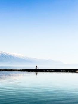 Scenic view of a cyclist riding on a pier at Lake Ohrid, surrounded by snow-capped mountains.