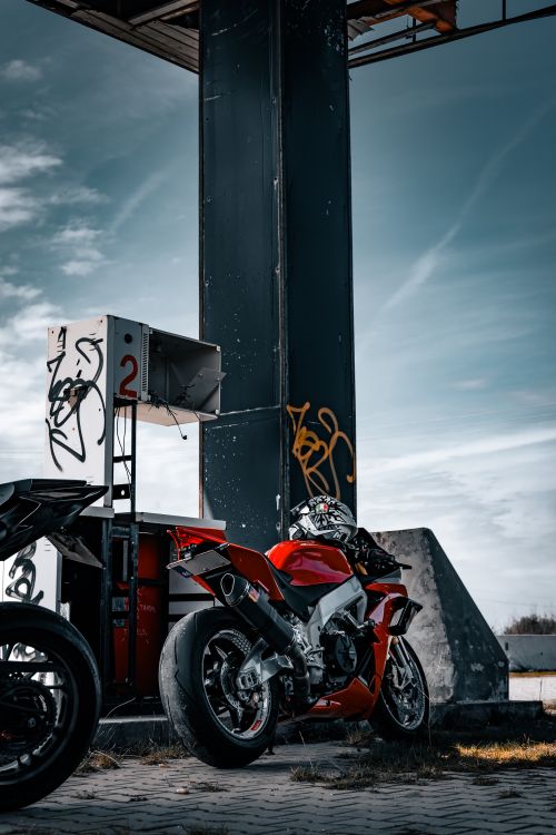 Free Bold red motorcycle parked at an urban gas station with graffiti under a moody sky. Stock Photo