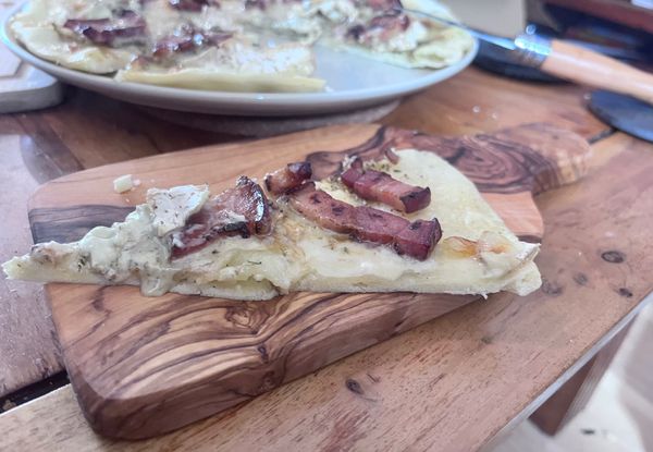 Part de pizza maison aux lardons sur une planche en bois d'olivier