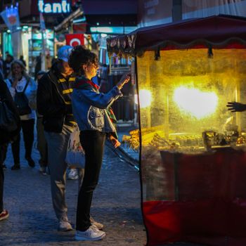 A woman buys roasted chestnuts from a street vendor in an outdoor marketplace at night.