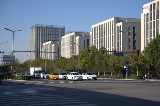 A city intersection with cars, traffic lights, and modern office buildings under a clear day sky.