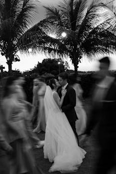 A romantic outdoor wedding captured in black and white, with a couple surrounded by blurred guests.