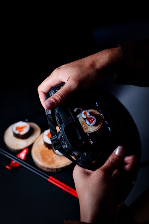 Free Close-up of a photographer taking pictures of gourmet sushi on wooden plates in a studio setting. Stock Photo