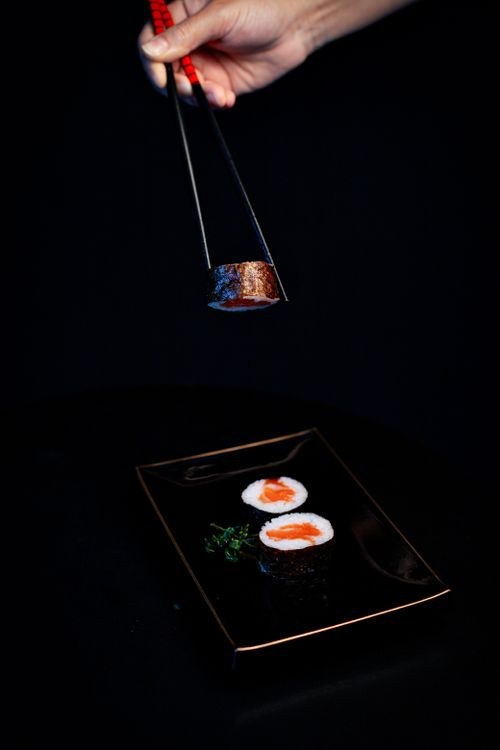 Free A meticulously crafted salmon sushi omakase piece held by chopsticks above a black plate, against a dark background. Stock Photo