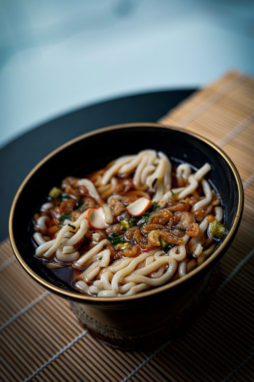 Free Savory udon noodles served in a black bowl with rich broth and garnishes. Stock Photo