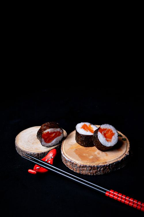 Free Fresh salmon sushi rolls displayed with chopsticks on a wooden platter against a dark background. Stock Photo
