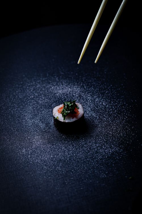 Free A single sushi roll artfully presented with chopsticks poised above, against a dark background. Stock Photo