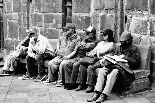 Free A black and white photo of people relaxing on benches in Quito, Ecuador, showcasing urban life. Stock Photo