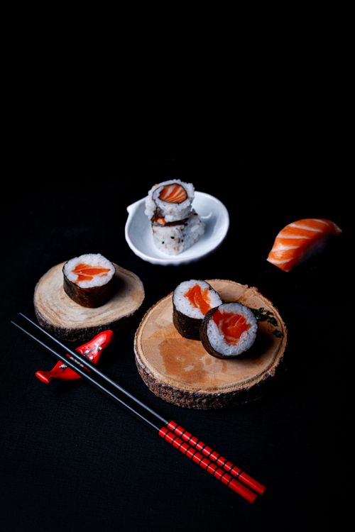 Free Artistic display of sushi rolls and salmon nigiri on wooden slices, black background. Stock Photo