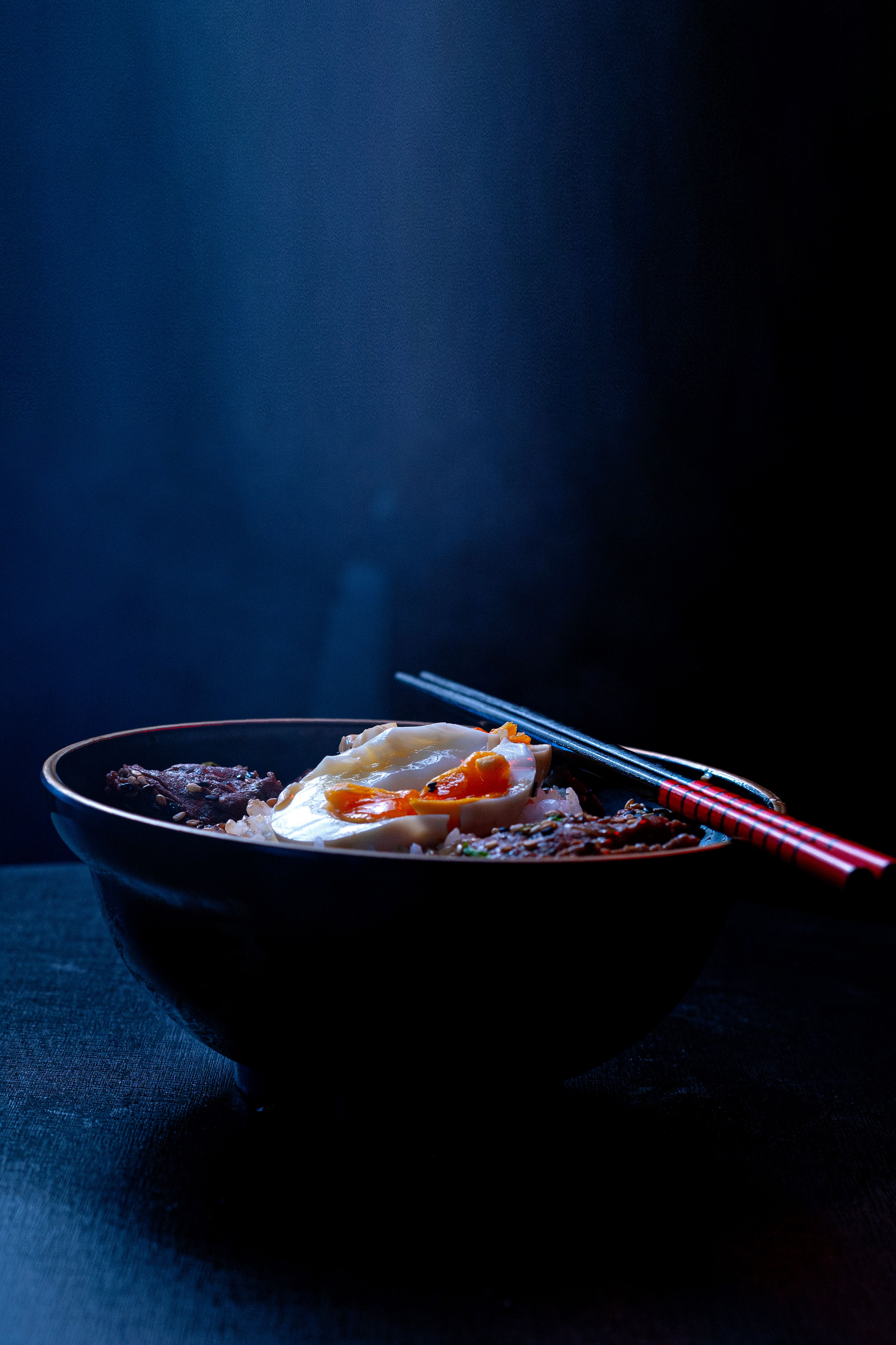 A flavorful Asian noodle bowl topped with beef, egg, and vegetables, artfully presented with chopsticks.