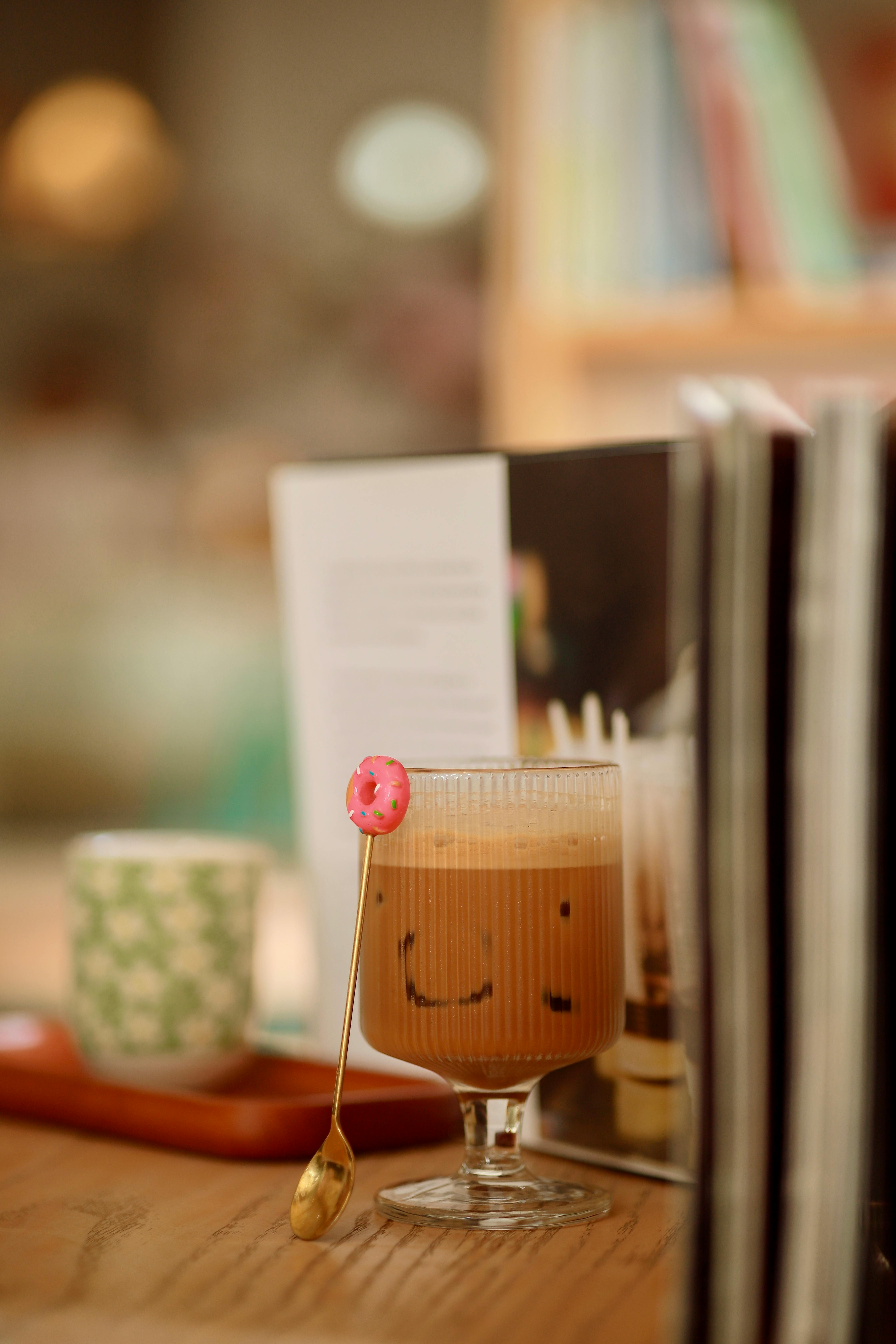 Kostenlos Eiskaffee mit einem lächelnden Gesicht, Donut und Büchern in einem gemütlichen Café-Ambiente. Stock-Foto