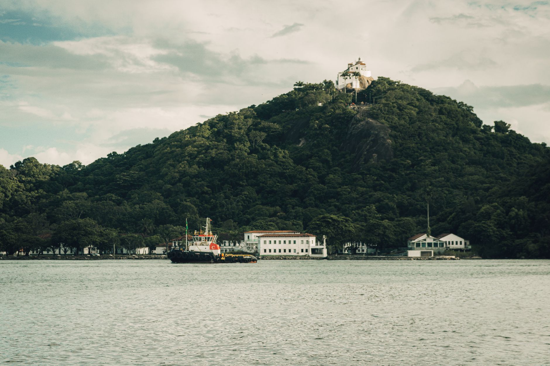 A tranquil scene featuring a boat and the historic Nossa Senhora da Penha Convent atop a lush hill.
