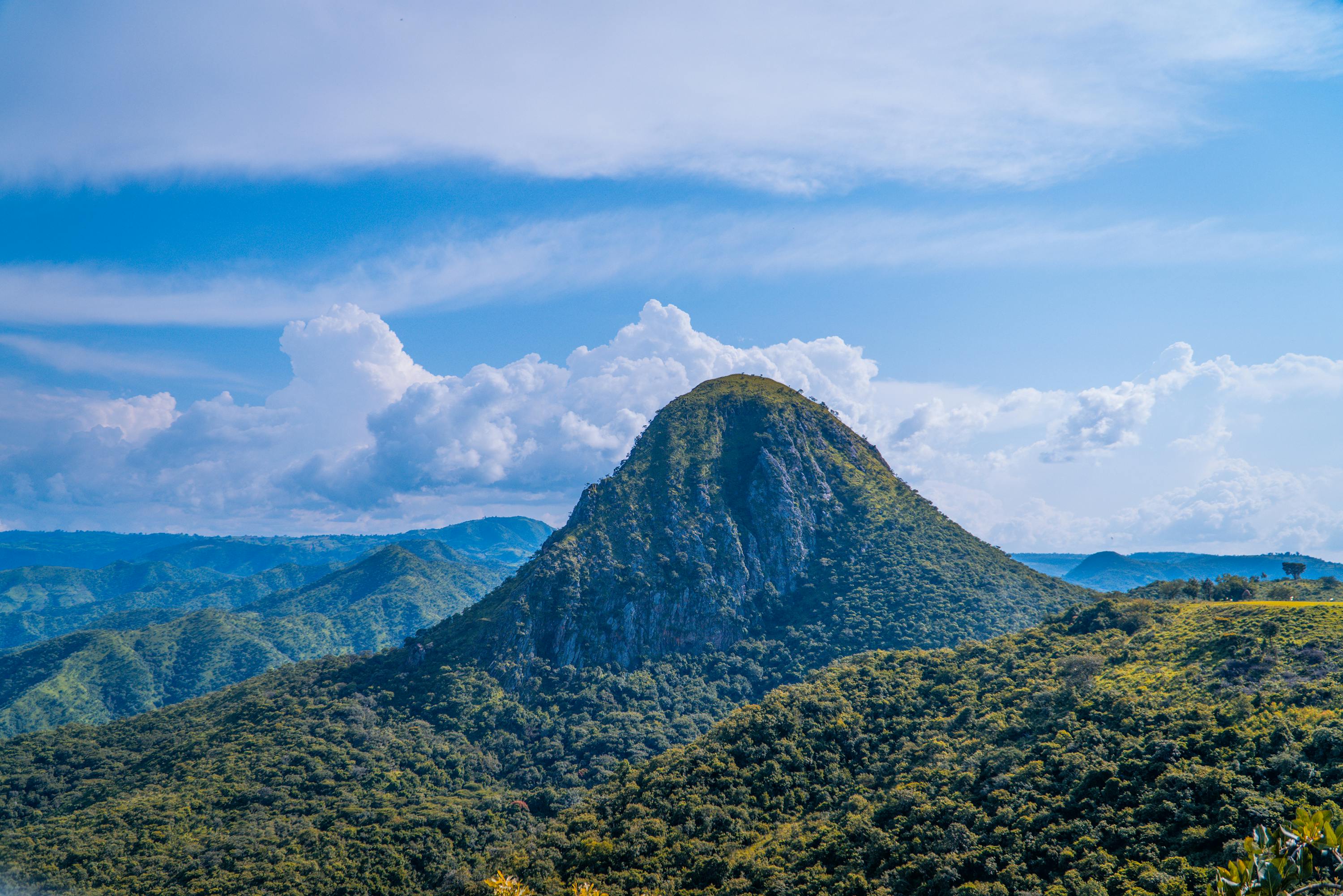 Beautiful green mountain landscape under a clear blue sky with fluffy clouds.