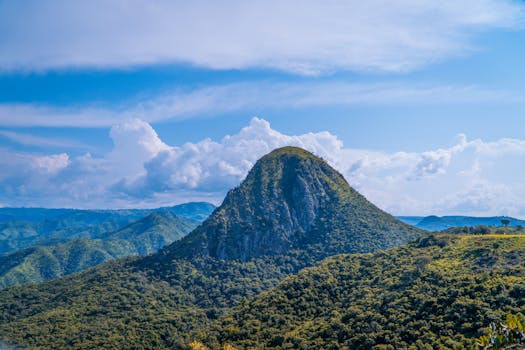 Beautiful green mountain landscape under a clear blue sky with fluffy clouds.