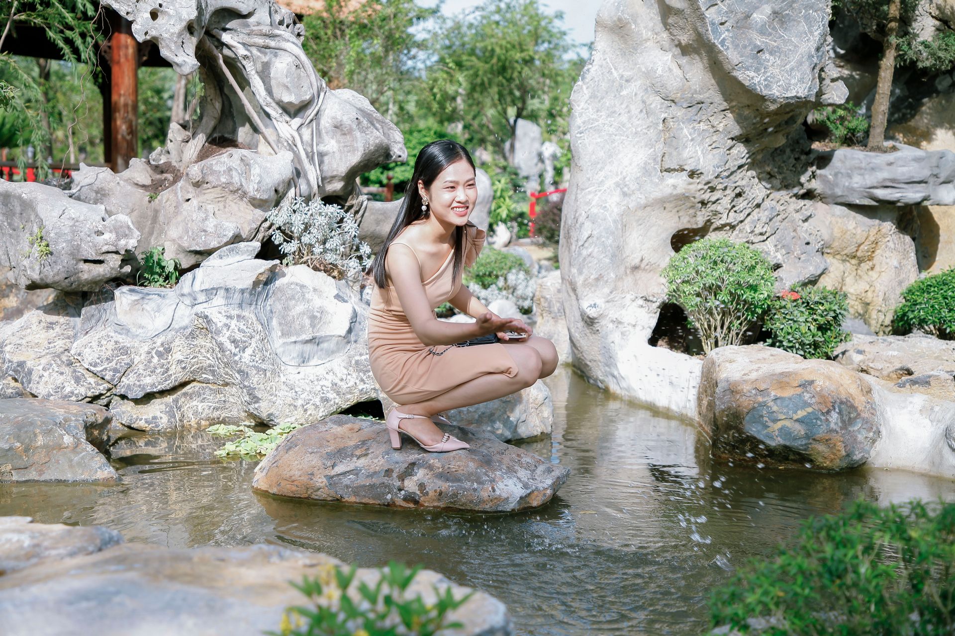 A woman sitting by a serene rock pool amidst lush garden scenery, exuding tranquility.