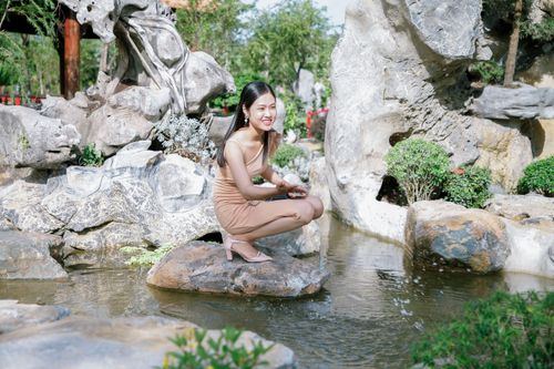 Free A woman sitting by a serene rock pool amidst lush garden scenery, exuding tranquility. Stock Photo