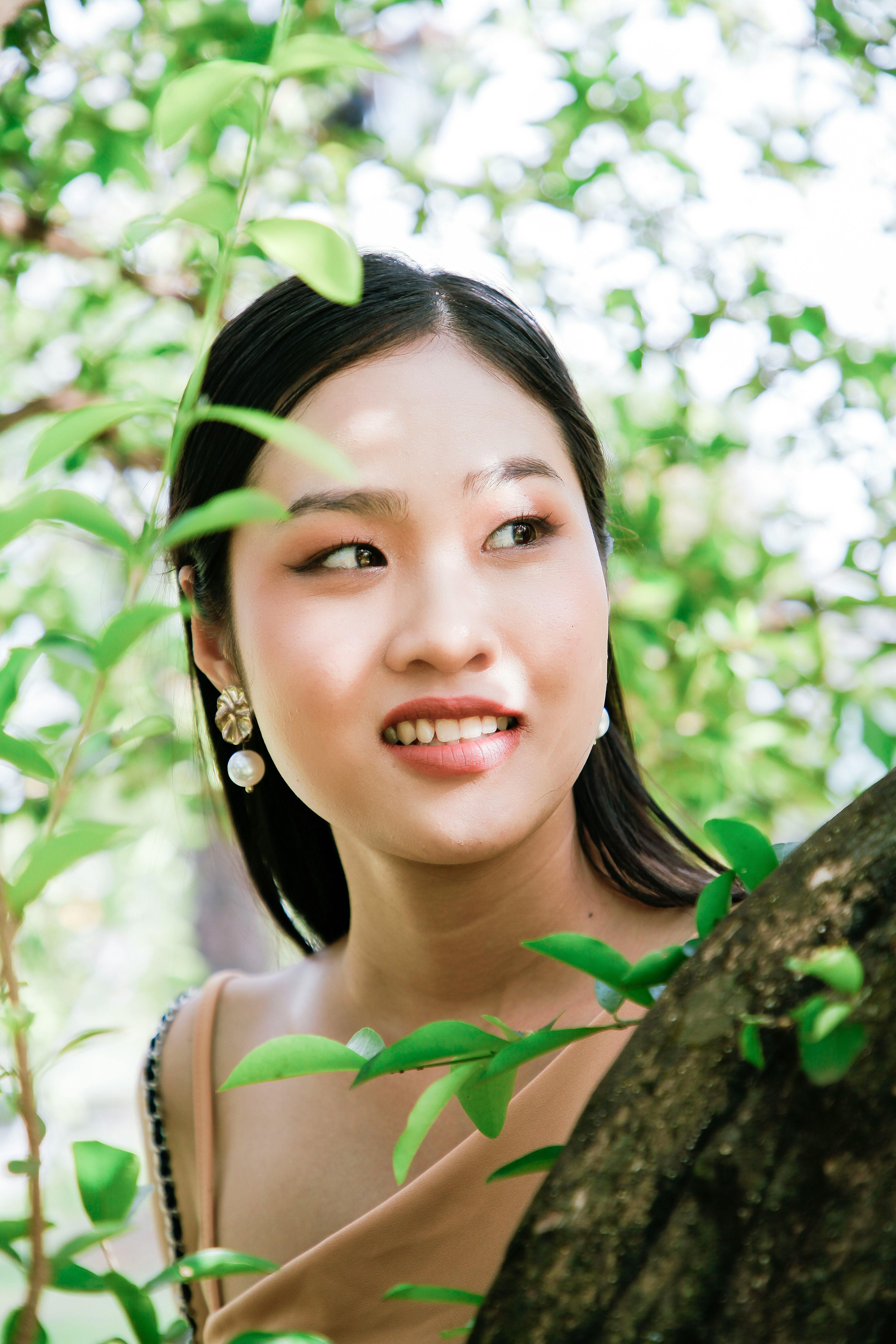 Portrait of a young woman surrounded by vibrant green leaves outdoors.
