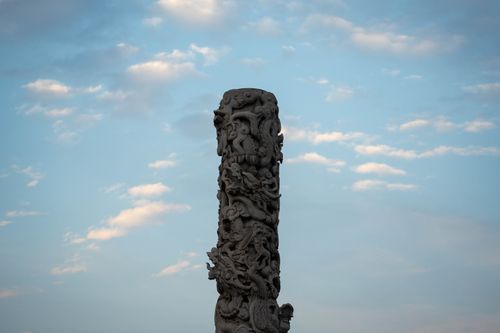 Free Artistic stone column with detailed carvings set against a serene blue sky with clouds. Stock Photo
